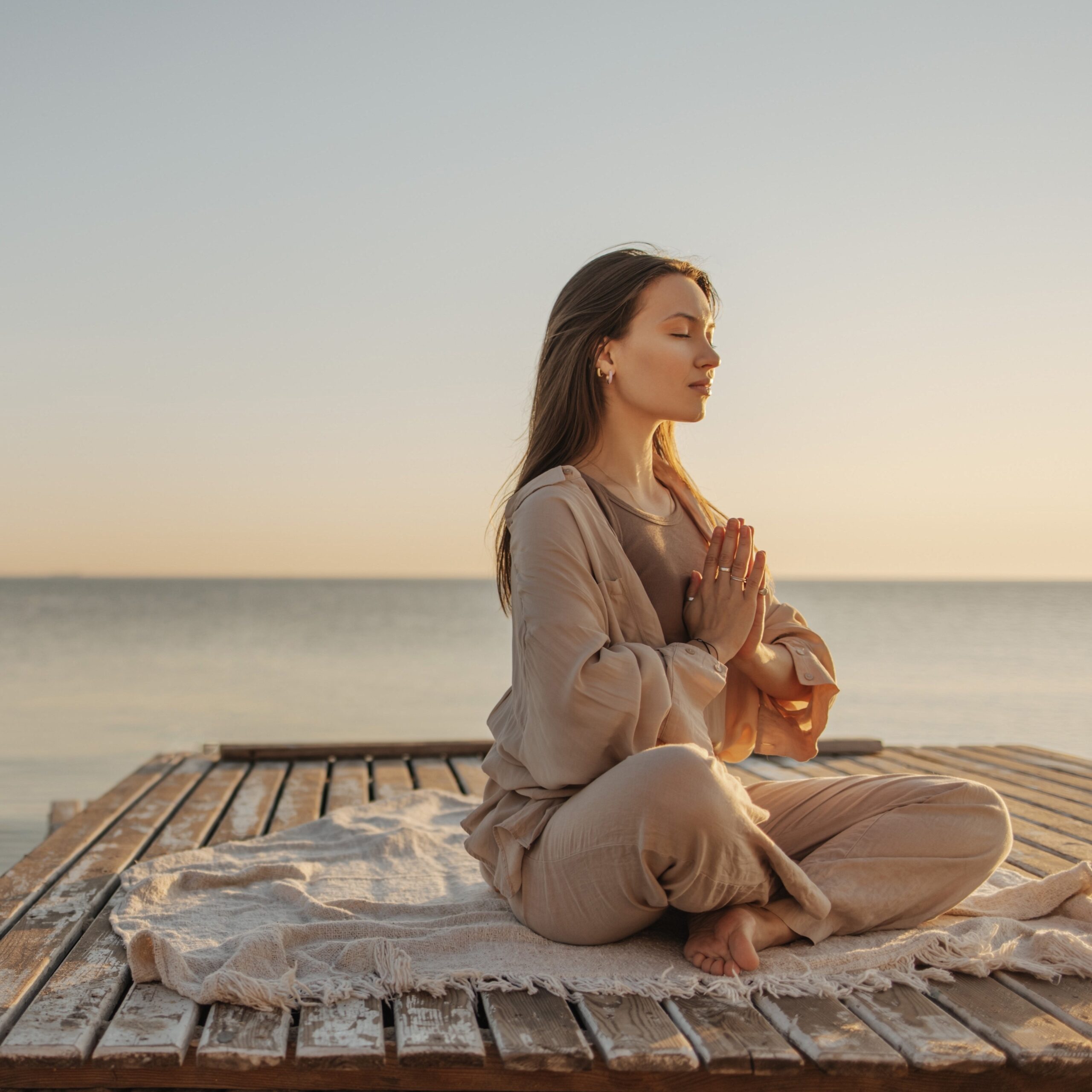 woman meditating on wooden pier by sea
